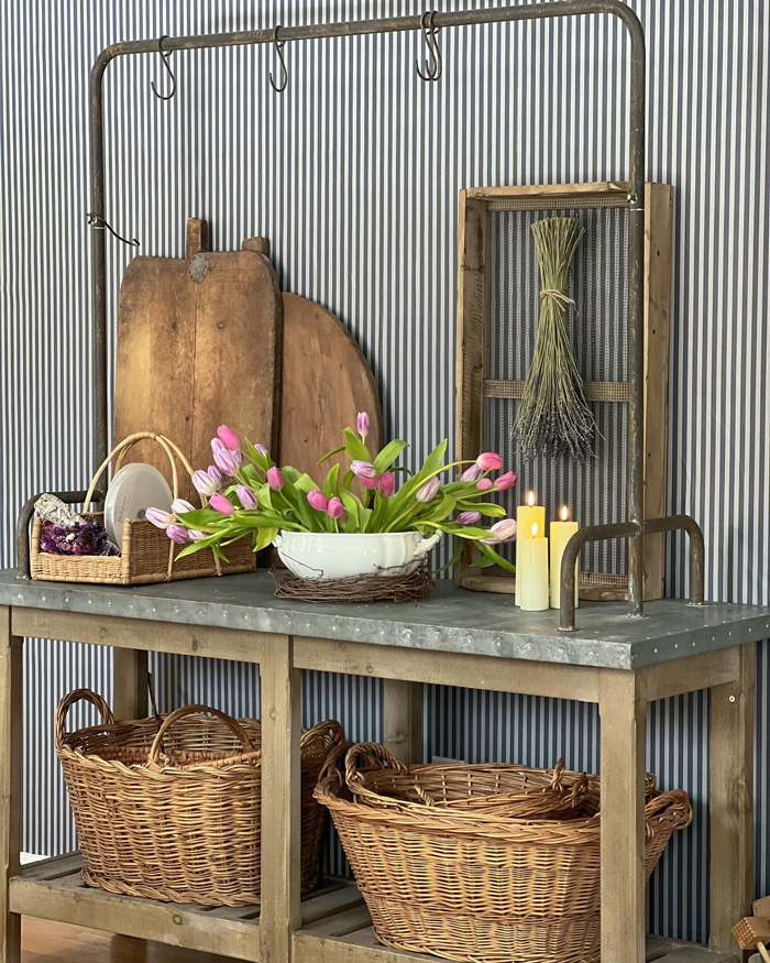 Striped removable wallpaper decor with baskets, wooden cutting boards, pink tulips in white bowl, and lit candles on wooden table.