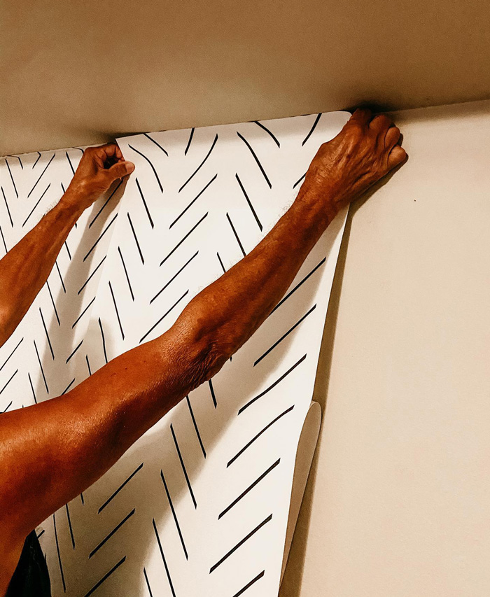 Person carefully hanging stylish removable wallpaper with black lines on a white background to decorate interior space.