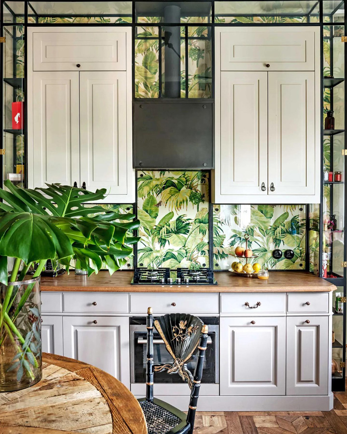 Kitchen with stylish removable wallpaper featuring green leaves behind white cabinets and wooden countertops.