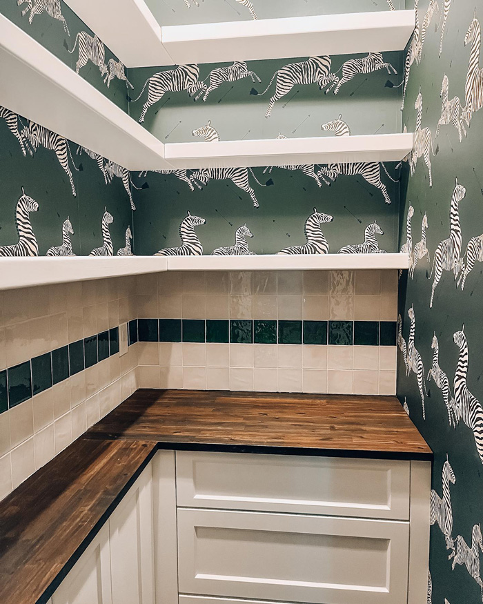 Green removable wallpaper with zebra patterns in a kitchen corner featuring wooden countertops and white cabinetry.