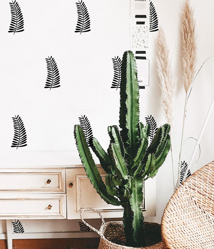White removable wallpaper with black leaf pattern behind a tall green cactus in a woven basket near a vintage cabinet.