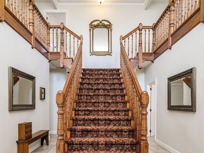 big wooden staircase with a vintage carpet inside an apartment with white walls