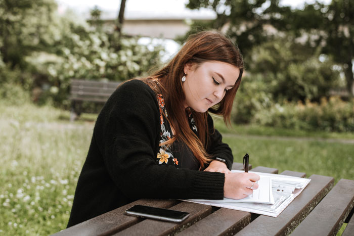 a concentrated woman writing notes in papers in the park