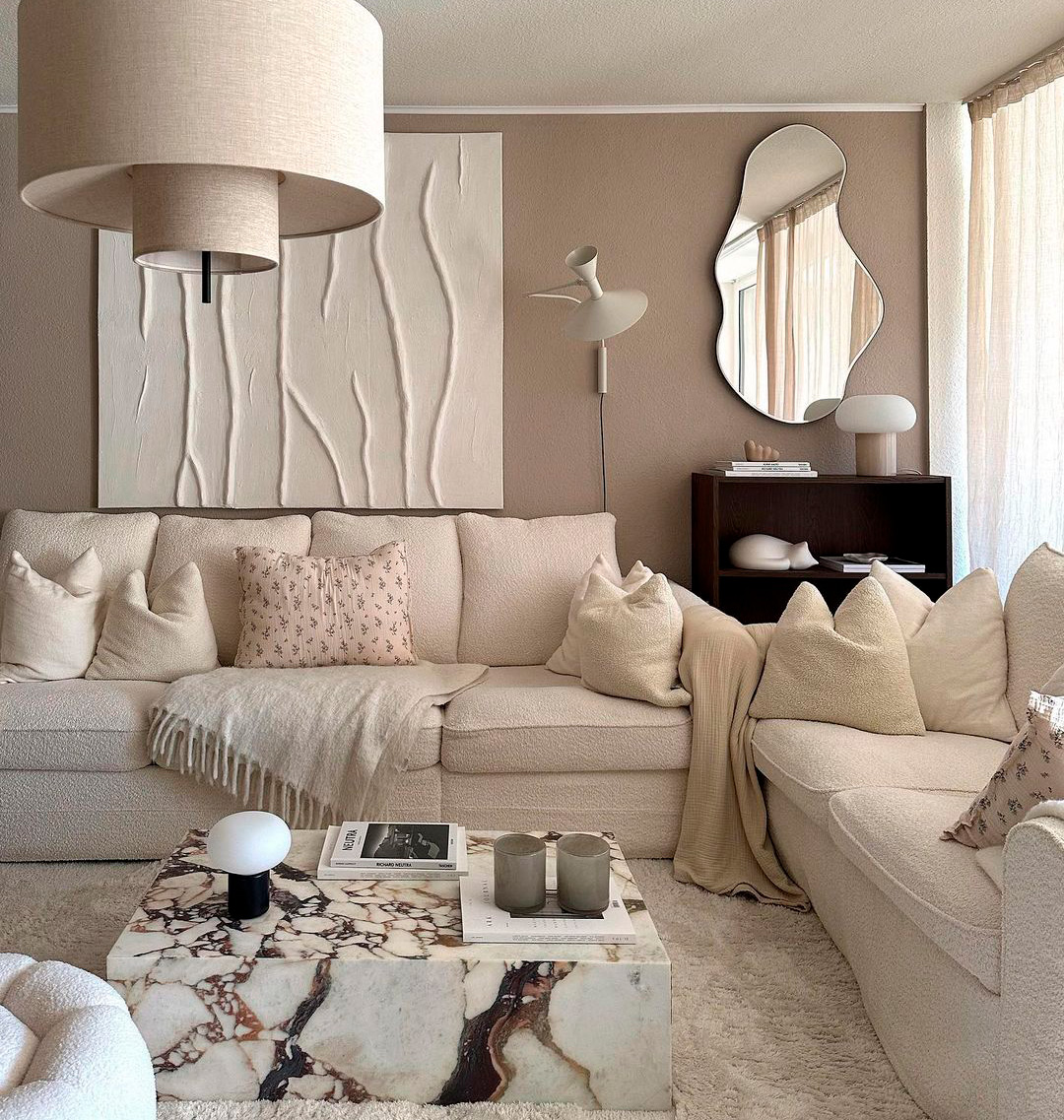 Living room with taupe walls, beige sofa, marble coffee table, and abstract mirror for a modern, cozy vibe.
