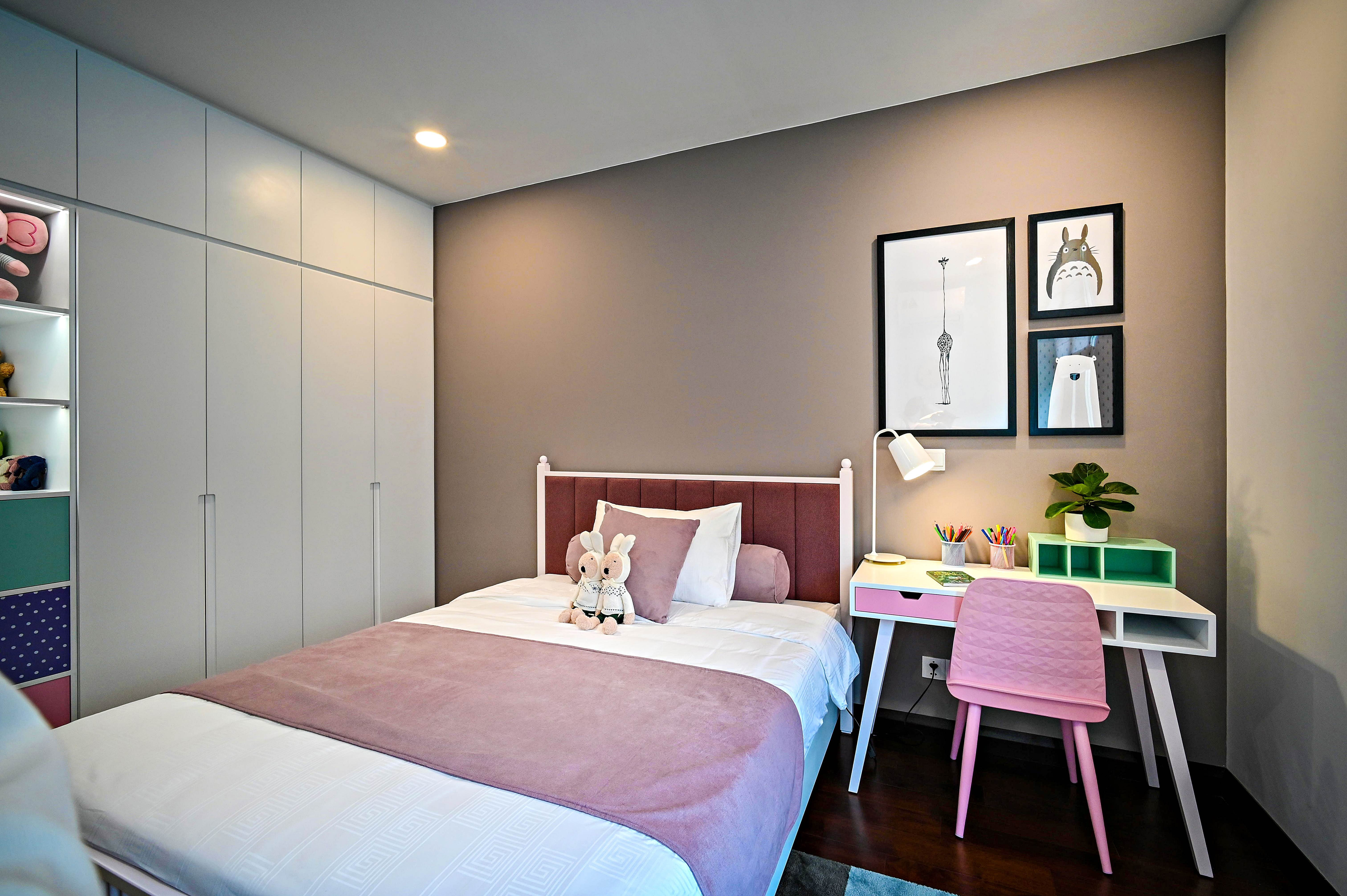 Bedroom with taupe walls, pink bedspread, and white desk featuring colorful decor and framed art prints.