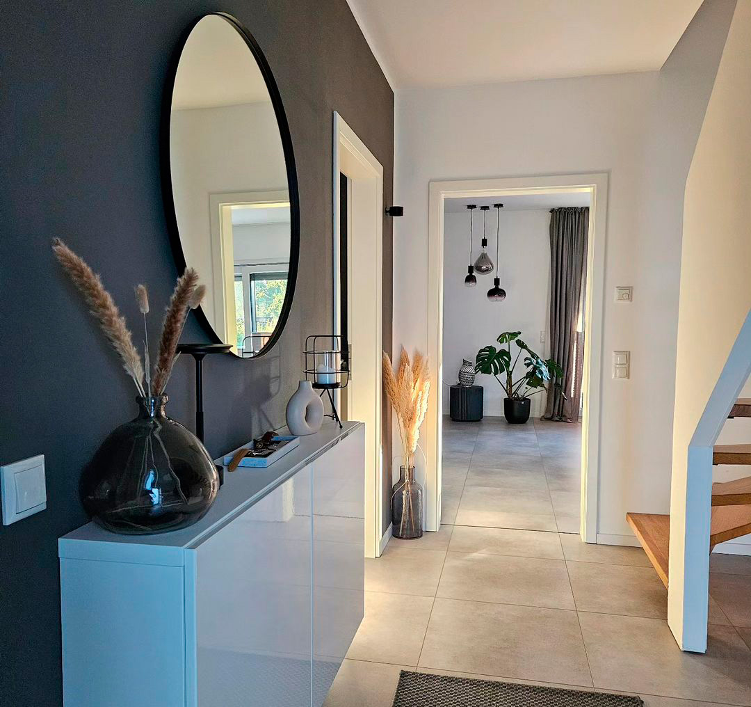 Modern hallway with taupe floor tiles, a round mirror, and elegant decor, leading to a room with hanging lights.