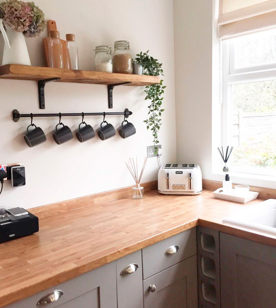 Taupe kitchen with wooden countertops, featuring a shelf with jars and mugs, creating a cozy and inviting space.