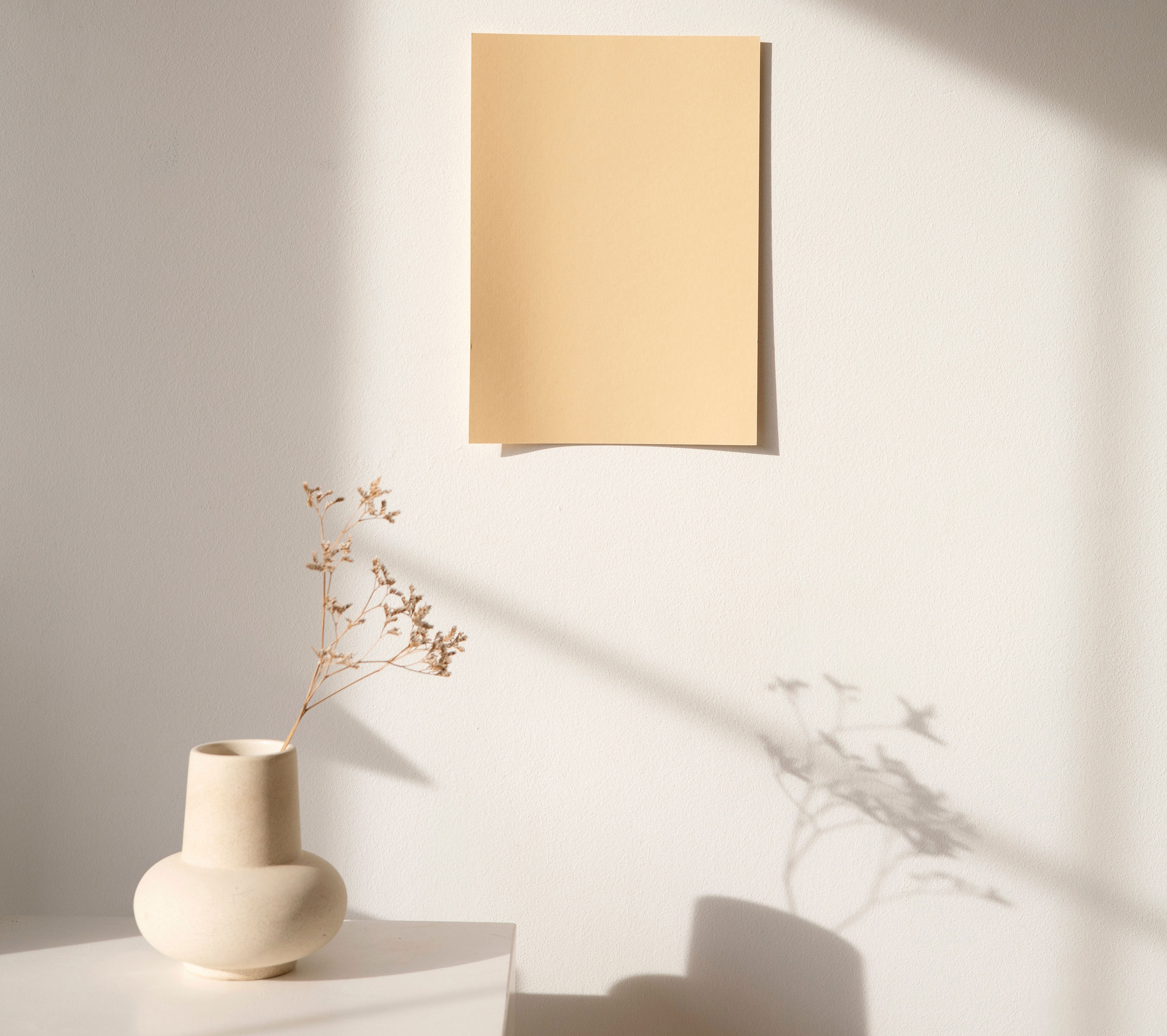 Taupe vase on a white table with dried flowers casting a shadow on a wall, showcasing taupe color use in decor.