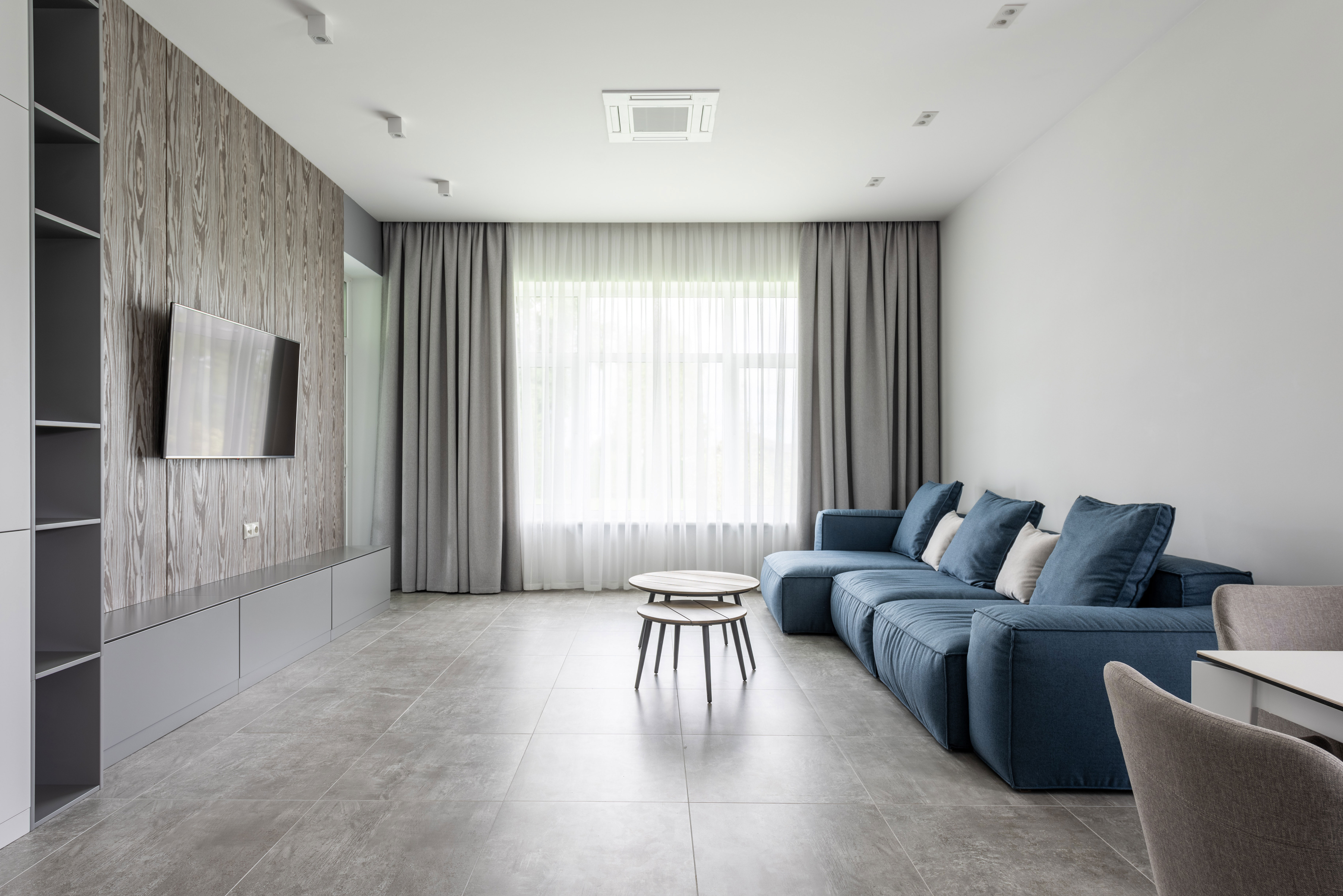 Modern living room with taupe curtains and walls, featuring a blue sofa and a sleek TV setup.