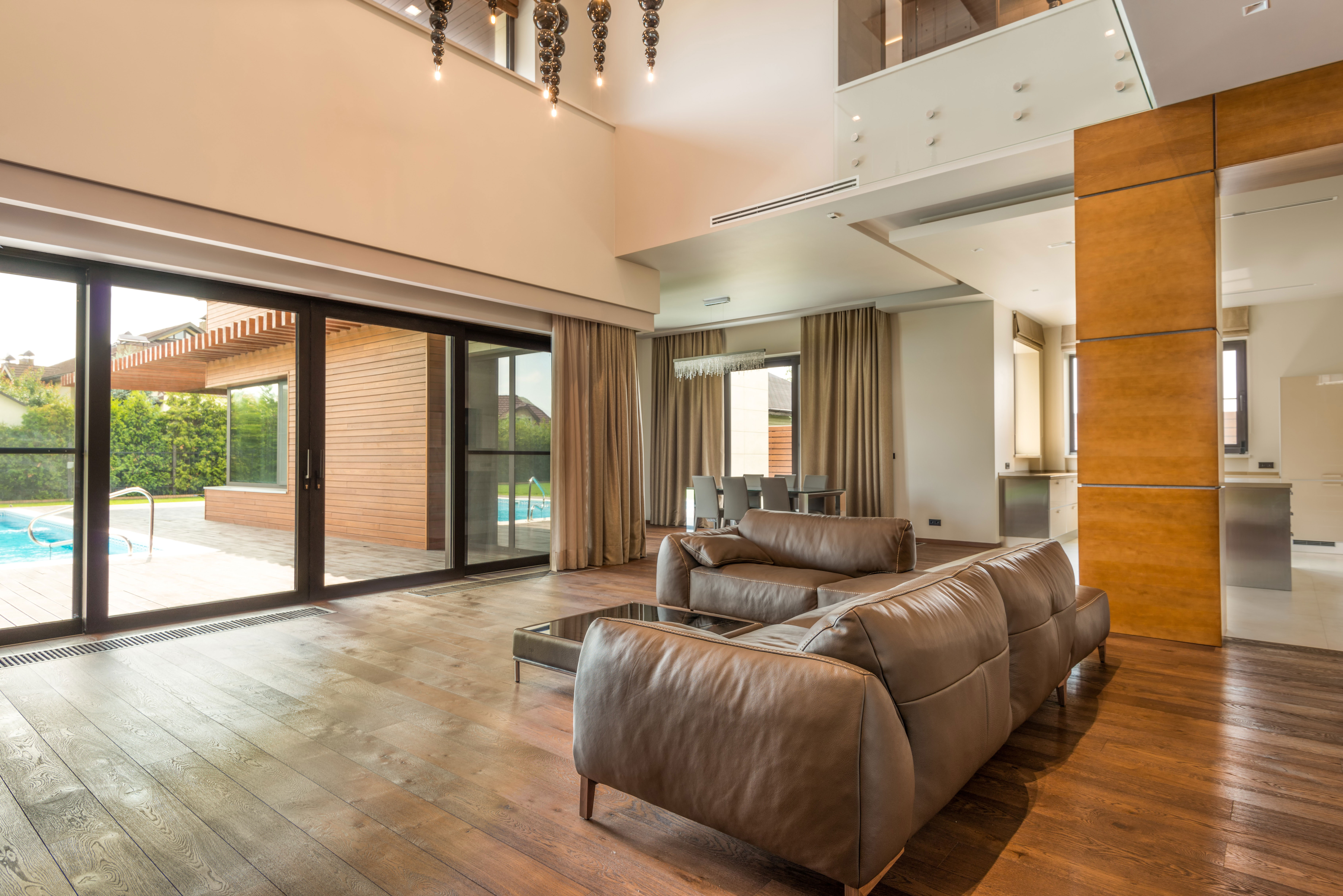 Spacious living room with taupe sofas, wooden flooring, and large windows overlooking a pool area.