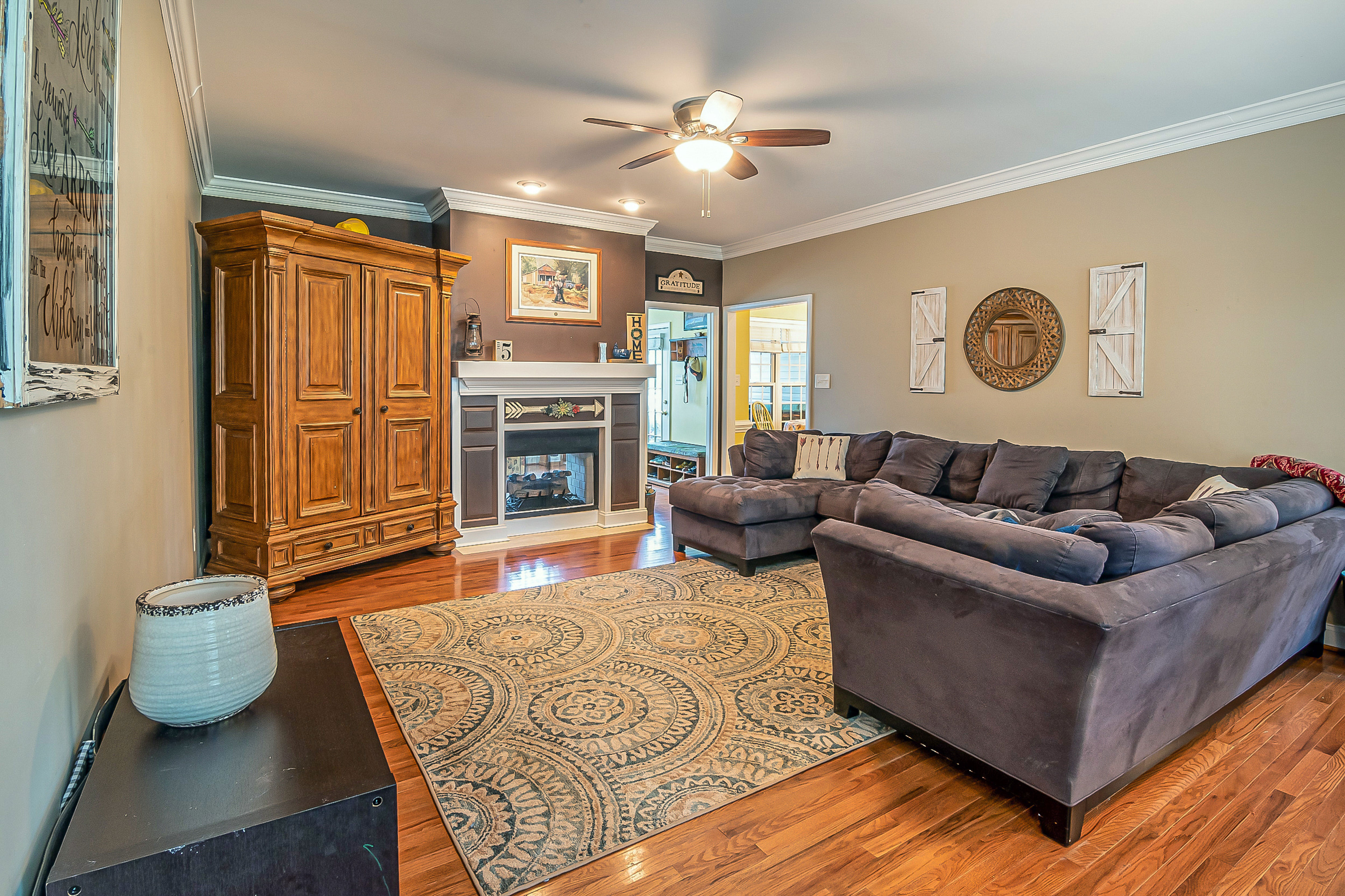 Taupe-colored living room with wooden floors, a large sectional sofa, and a fireplace, creating a cozy atmosphere.