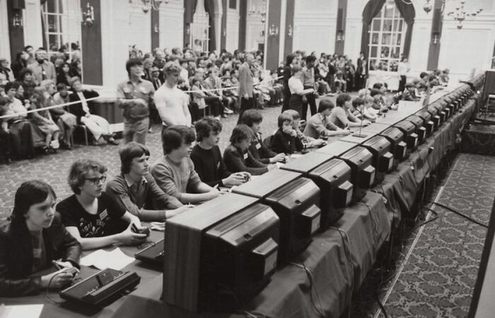 Black and white historical photo of young people seated in a row using vintage computers at a public event.