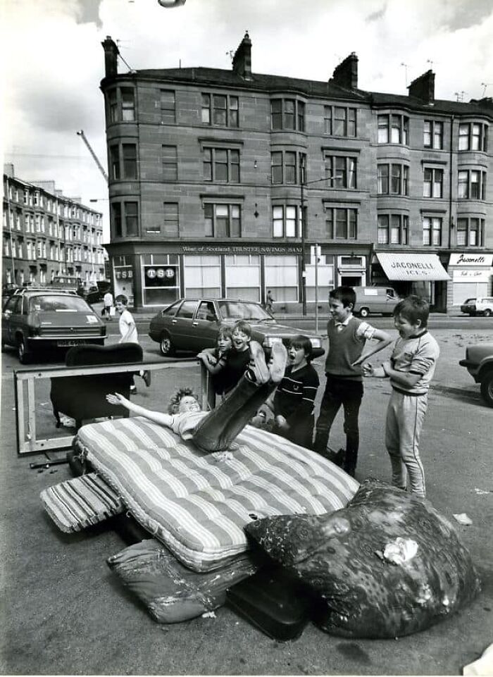 Group of children playing on a mattress on the street in a historical photo showing urban life decades ago.