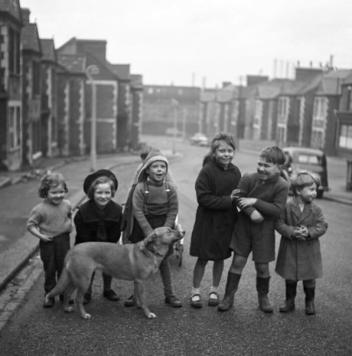 Group of children and a dog playing on a street in a historical black and white photo from past decades.