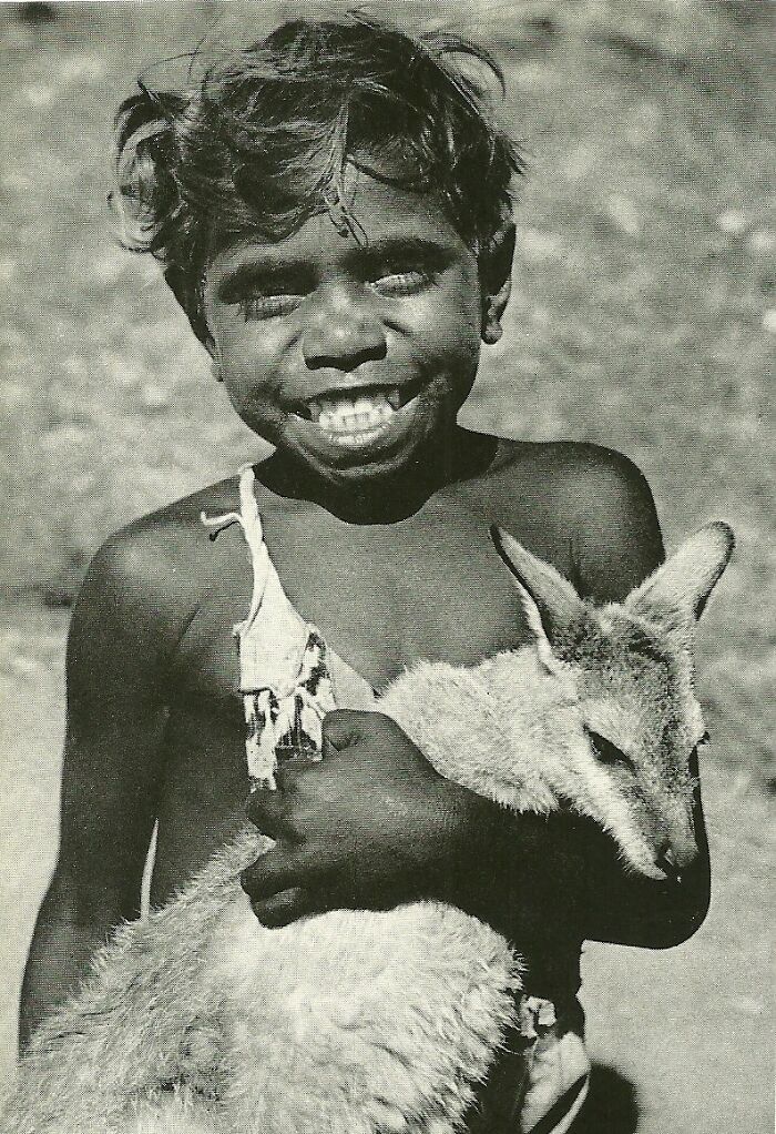 Smiling young boy holding a kangaroo in a black and white historical photo capturing a moment of joy and connection.