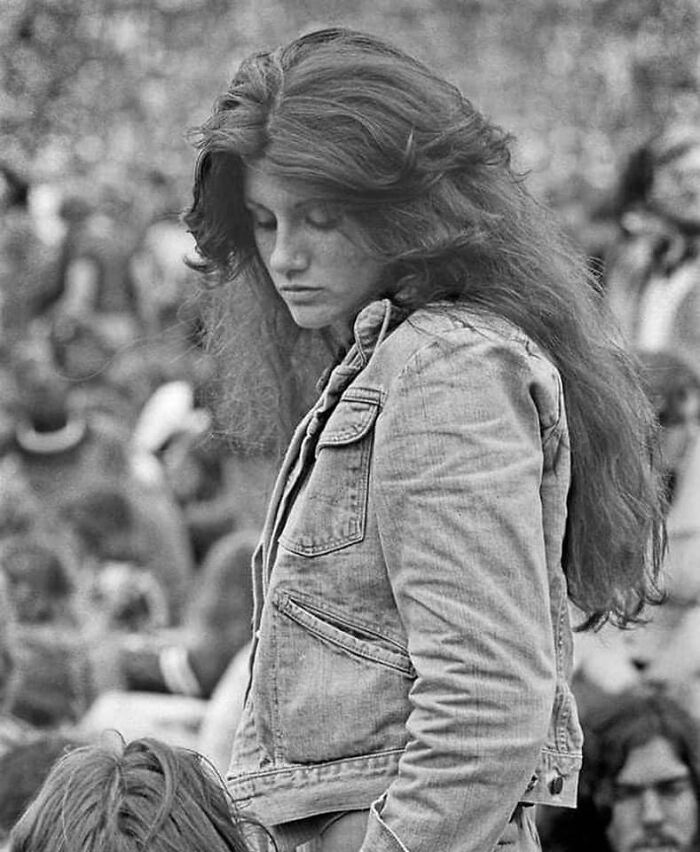 Young woman with long hair wearing a denim jacket at an outdoor event, a rare historical photo showing 1970s fashion.