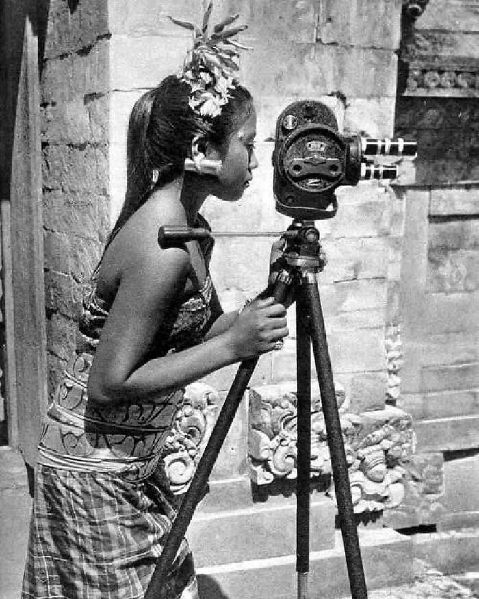 Young woman in traditional dress using vintage camera on tripod in a historical photo from the past era.