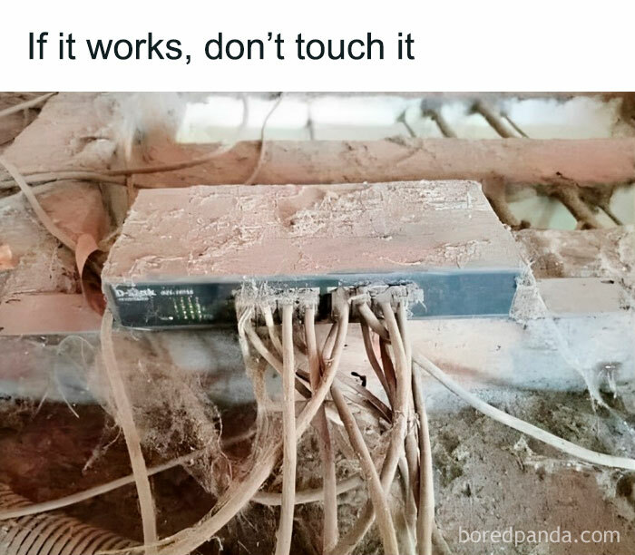 Dusty network switch covered in cables with text "If it works, don’t touch it," depicting a humorous engineering meme.