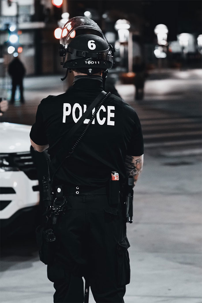 Police officer in riot gear standing on an urban street at night, illustrating what not to do when visiting the US.