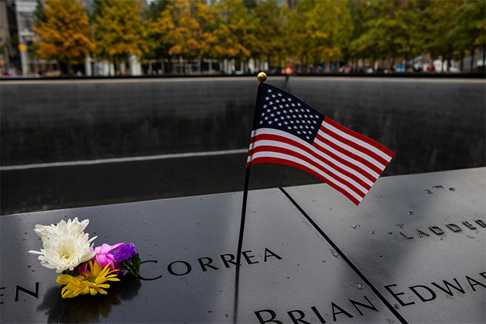 American flag and flowers placed on a memorial engraved with names, representing travel tips on what not to do when visiting the US.