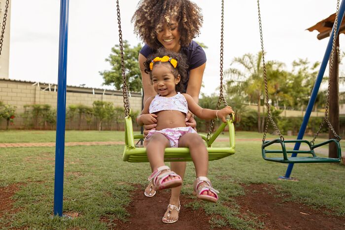 Mother pushing her smiling toddler on a swing in a park, capturing a joyful moment of unspoken mom code.
