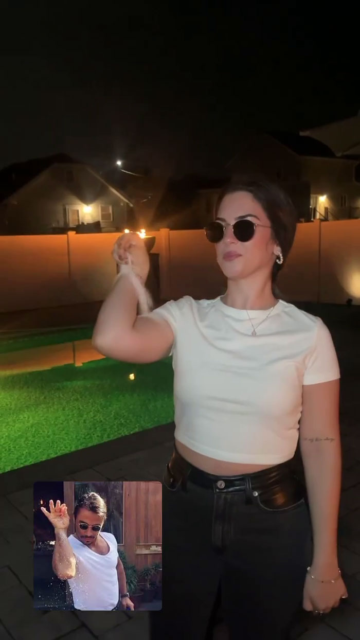 Woman at meme-themed party mimicking a famous meme pose in sunglasses and white top.