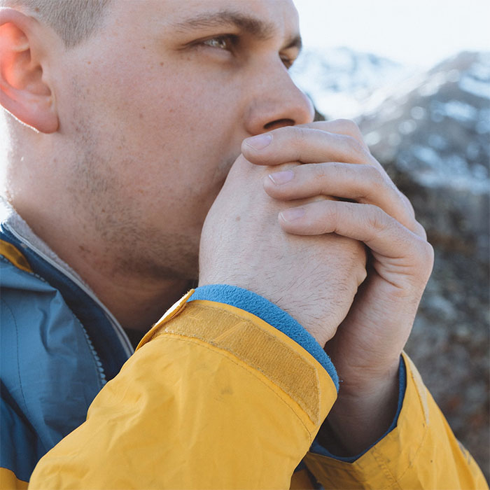 Close-up of a man in a yellow jacket warming his hands outdoors, illustrating life-saving tips when visiting the US.