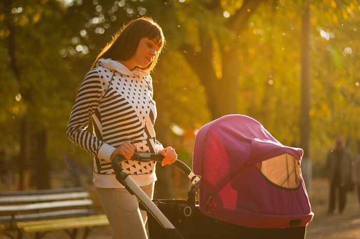 Mother pushing a stroller outdoors during golden hour, reflecting the unspoken mom code in a peaceful park setting.