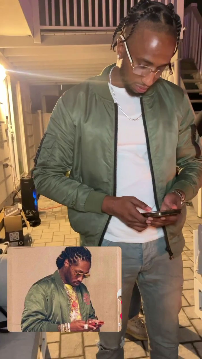 Man at meme-themed party in green jacket, mimicking a popular image on his phone screen.