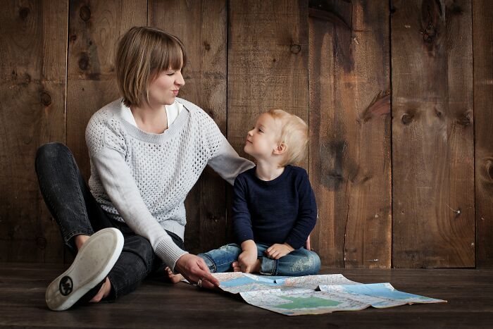 Mother and child sitting on floor looking at each other with a map, illustrating unspoken mom code connection.