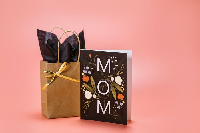 Mom card with floral design next to a gift bag with gold ribbon, symbolizing unspoken mom code and motherhood.