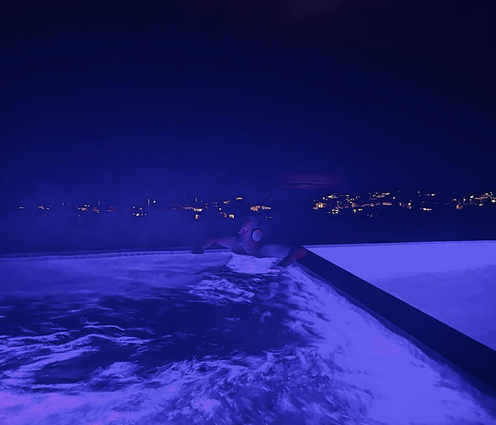 Man in a pool at night, surrounded by city lights, creating a mysterious atmosphere with Batman references.