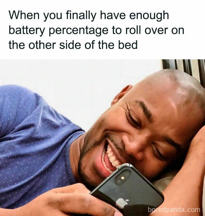 Man laughing at relatable funny meme on phone about life while lying in bed.