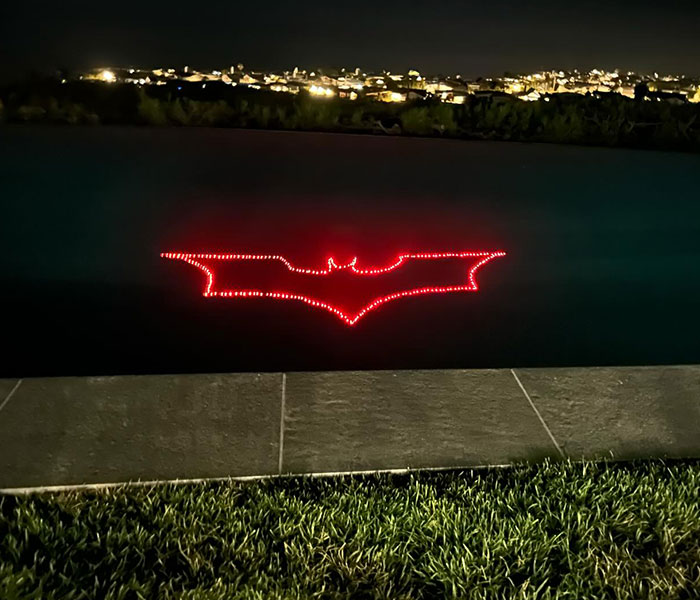 Red Batman logo glowing against a city nightscape backdrop.