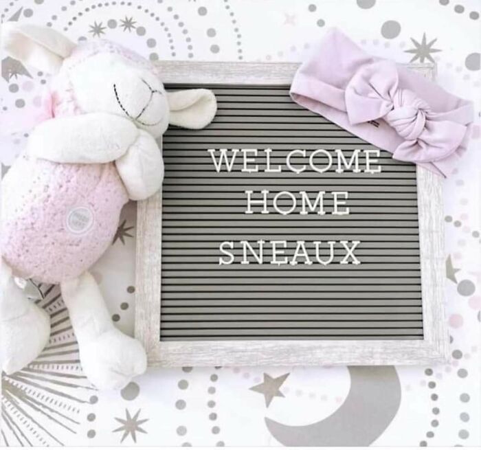 Welcome home sign with unique baby name "Sneaux" beside a plush lamb and pink headband.