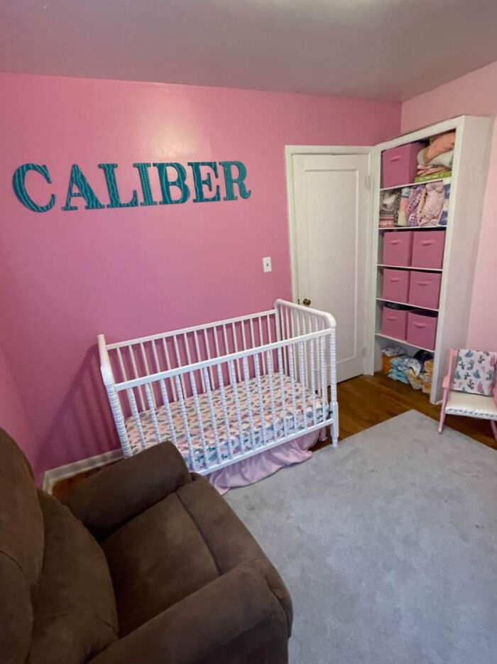 Pink nursery room with the name "CALIBER" on the wall, featuring a white crib and shelves with pink storage bins.