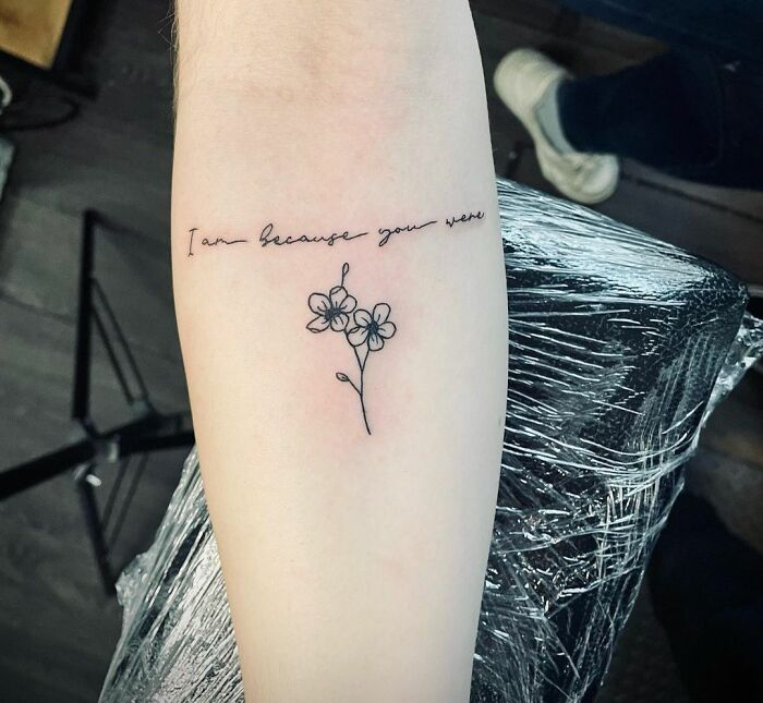 Minimalist floral tattoo with sentimental family tribute text on inner forearm.