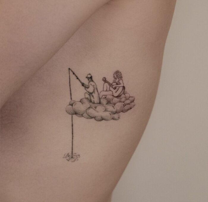 Tattoo of two people sitting on clouds, one fishing and one playing guitar, symbolizing family togetherness.