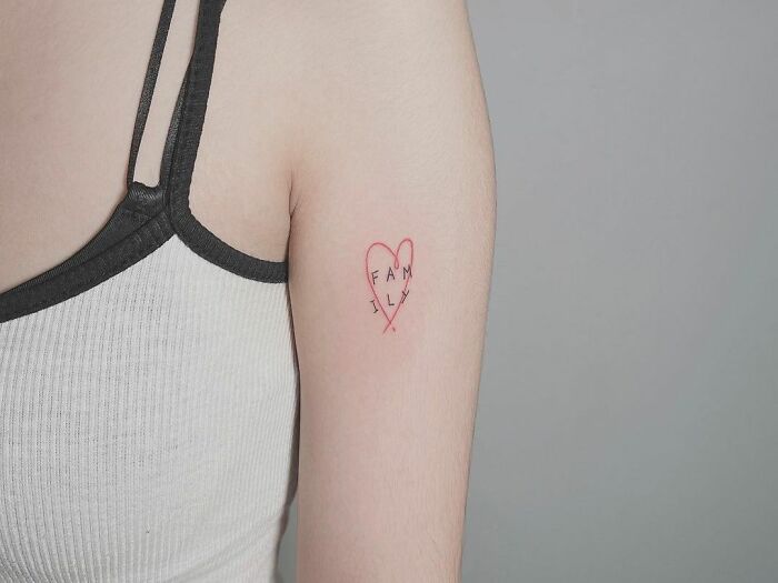 Tattoo with heart and "family" text on upper arm, honoring loved ones.