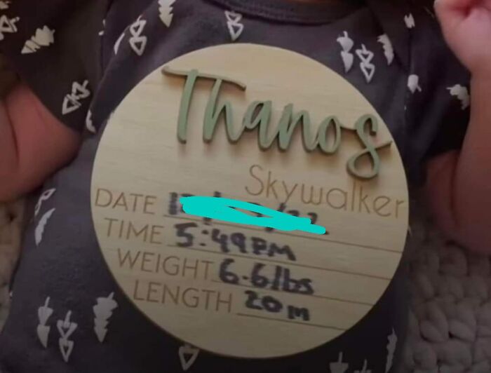 Baby with a personalized name card displaying "Thanos Skywalker" and birth details, showcasing a unique baby name choice.