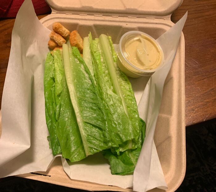 Cursed meme featuring an unconventional Caesar salad with lettuce, croutons, and dressing in a takeout box.