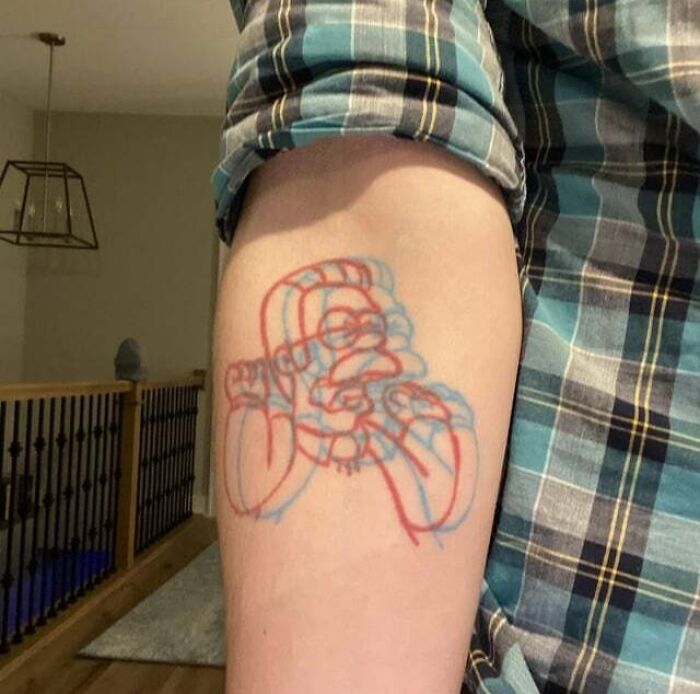 '90s culture tattoo showcasing iconic character in blue and red outline on a person's arm, plaid shirt visible.