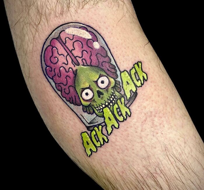 Colorful '90s tattoo with a green alien skull and exposed brain, featuring the text "Ack Ack" in yellow.
