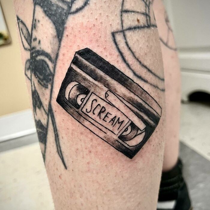 '90s tattoo depicting a VHS tape labeled "Scream" on a person's leg.