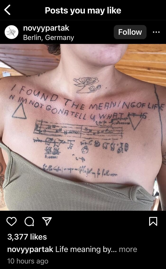 Close-up of a person's chest with humorous, handwritten tattoos about life's meaning.