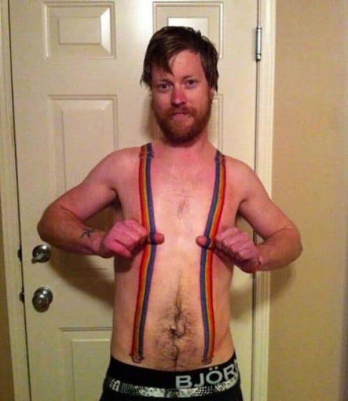 A man displays a colorful tattoo resembling rainbow suspenders on his chest, showcasing unique tattoo art.