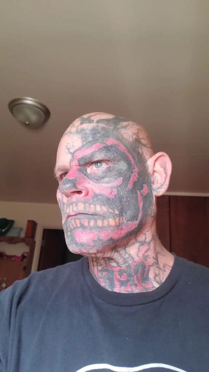 Man with a vividly detailed face tattoo featuring red and black skull design.