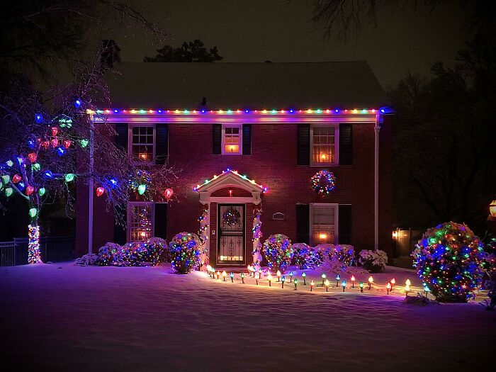 House decorated with colorful affordable Christmas lights outdoors during winter night with snow-covered ground.
