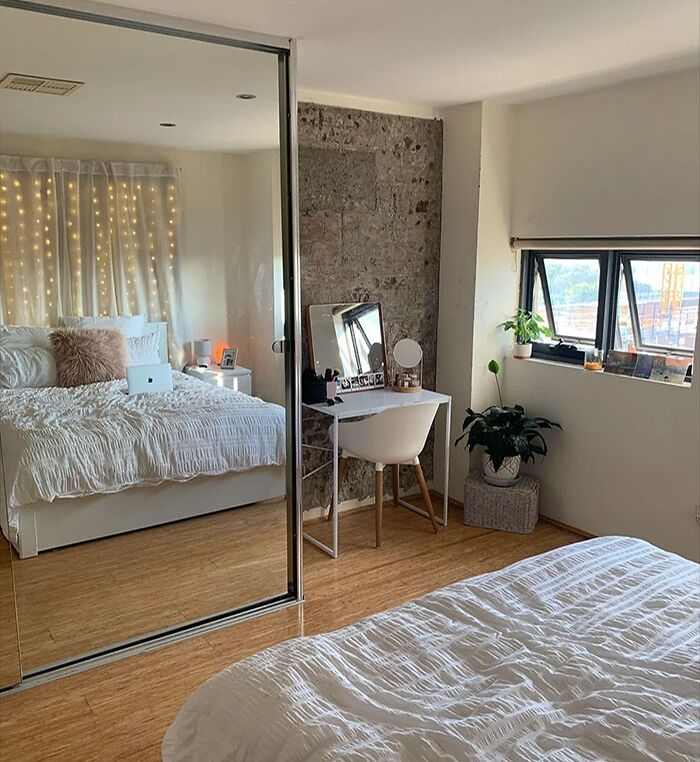 Cozy bedroom featuring oversized mirror wall decor, a white bed with string lights, and a small vanity desk with plants.