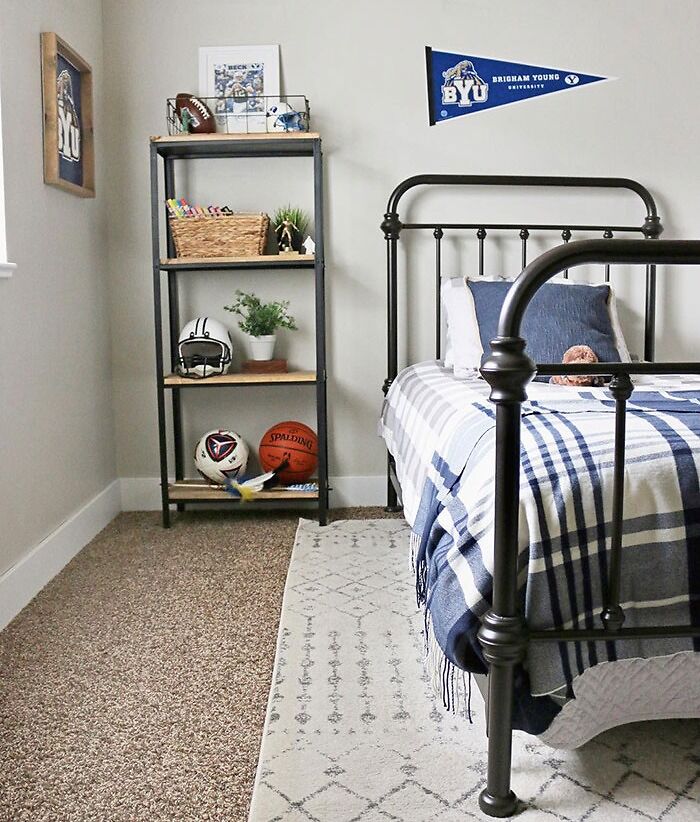 Sport-inspired bedroom wall decor with basketball, football gear, and university pennant above metal framed bed.